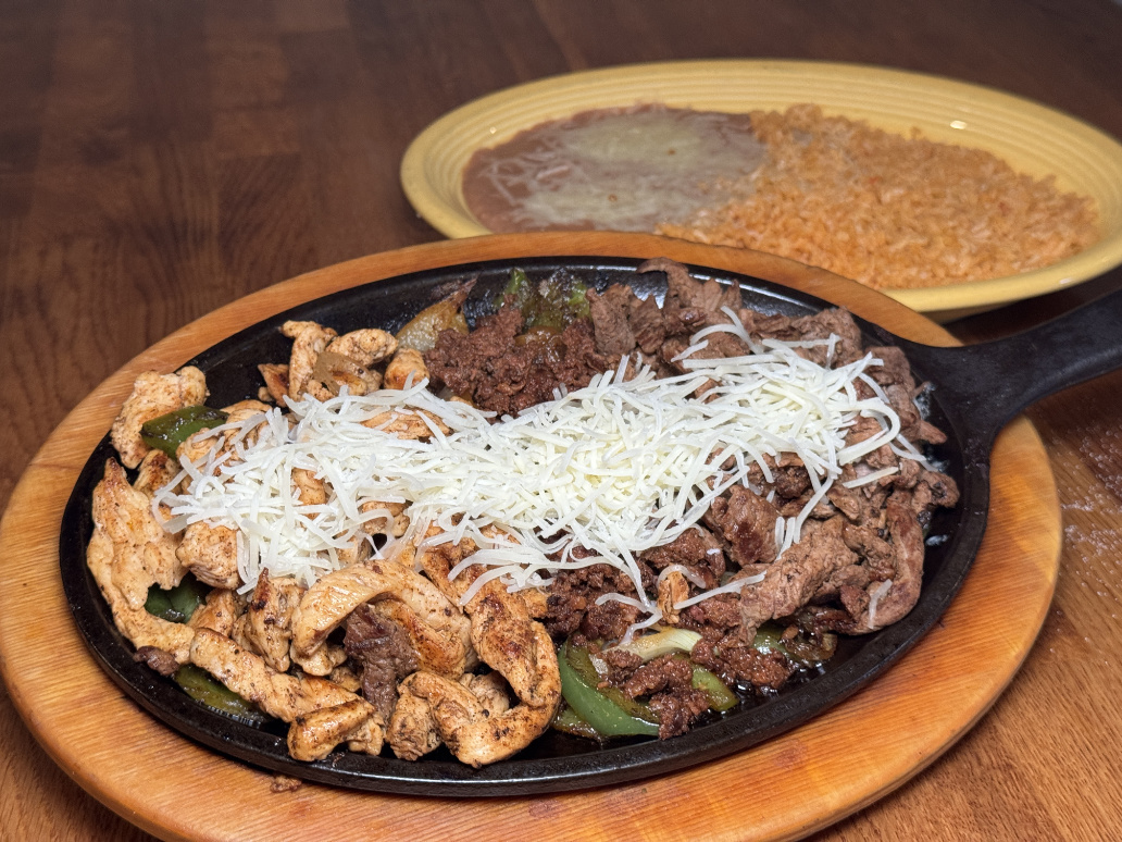 Sizzling fajitas with chicken and steak on cast iron skillet