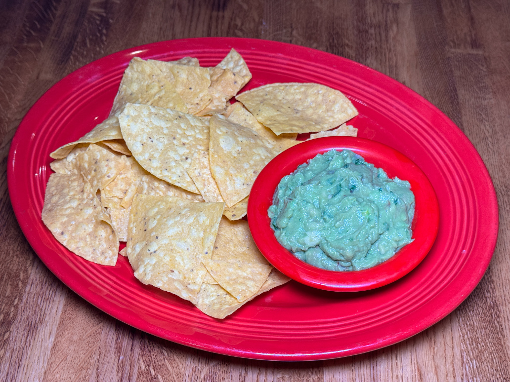 Fresh guacamole with tortilla chips on red plate